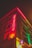 A multistory building is illuminated with colorful neon lights. The sign vertically spells out 'HOTEL DE FRANCE', using vibrant red and yellow hues. The glow from the signage reflects onto the building’s façade, giving it a lively and warm appearance. A small circular sign at street level reads 'INTER-HOTEL'. The night sky and street lighting add to an atmospheric urban ambiance.