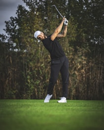 a man swinging a golf club on top of a green field