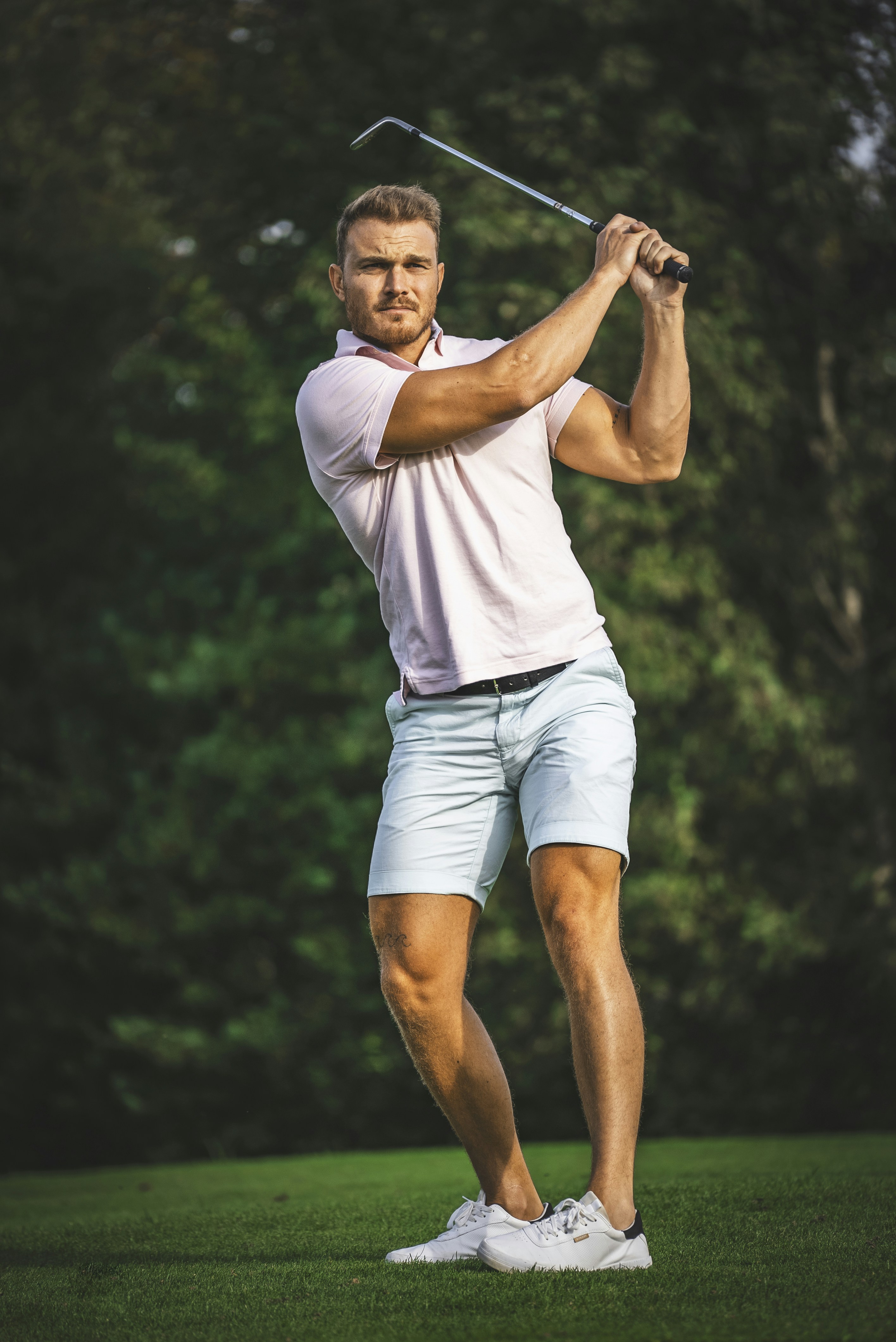 Bayou Heritage Polo worn on a golf course, model in action swing pose, green fairway background