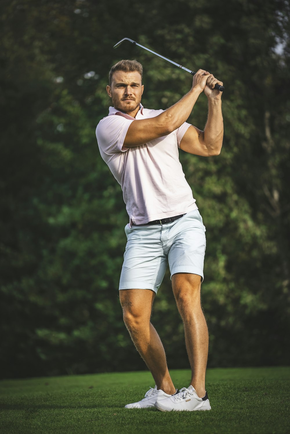 um homem balançando um taco de golfe em um campo verde exuberante