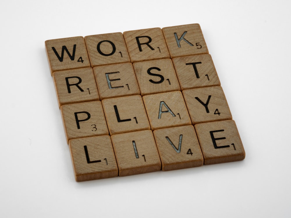 a scrabble tile with words that spell out work rest play live