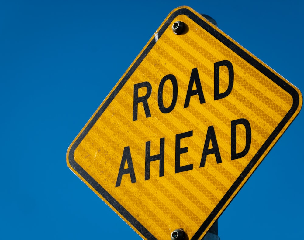 a road ahead sign with a blue sky in the background