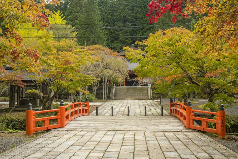 an orange bridge over a brick walkway surrounded by trees