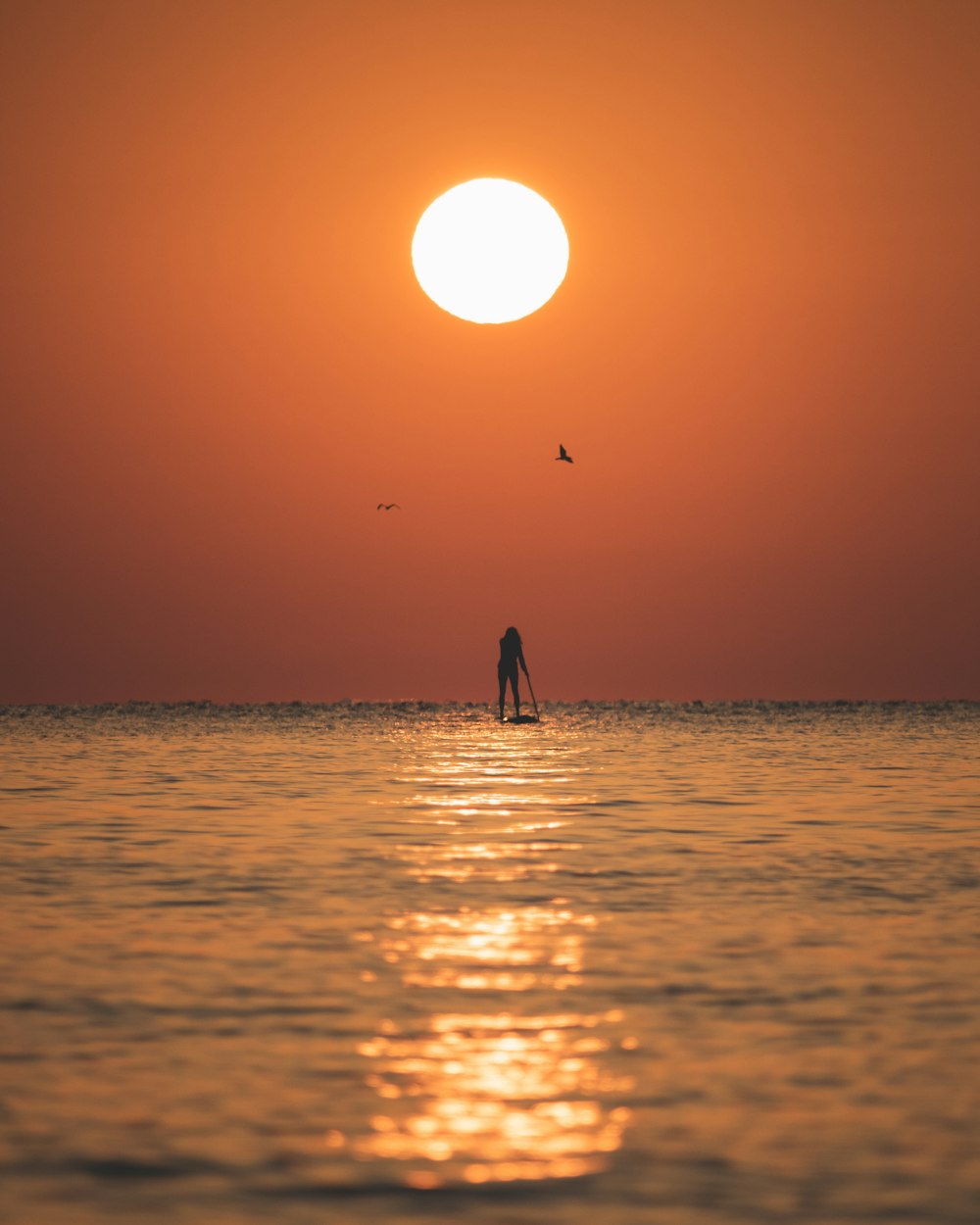 a person standing on a surfboard in the ocean at sunset