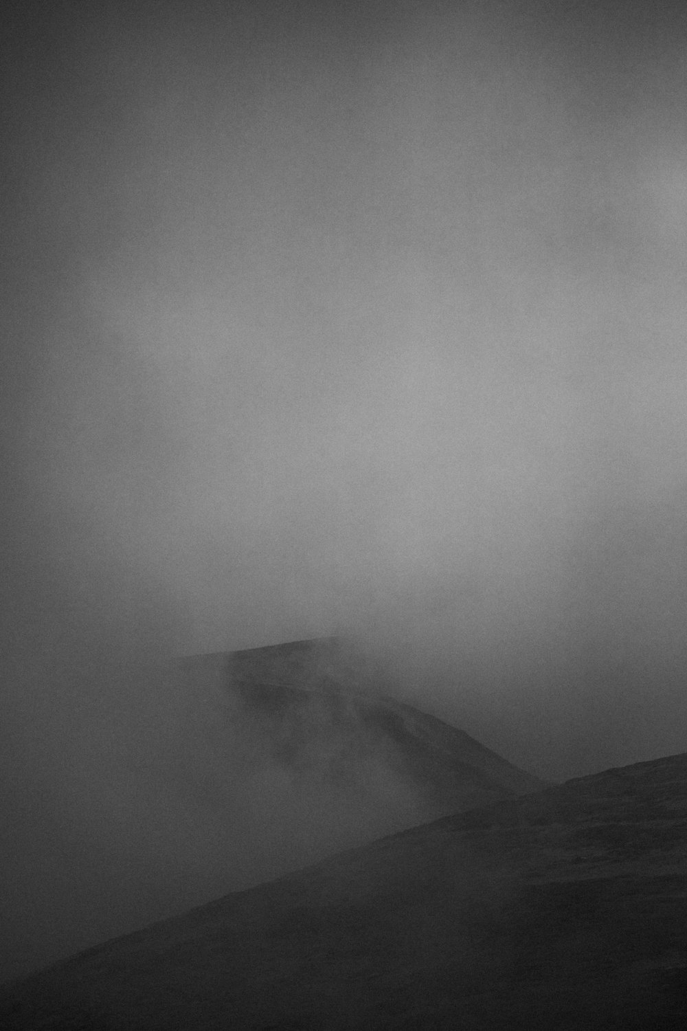 a black and white photo of a foggy mountain