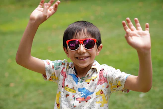 a young boy wearing sunglasses and waving his hands