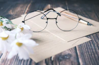 A pair of modern eyeglasses displayed on a wooden table surrounded by fresh flowers.