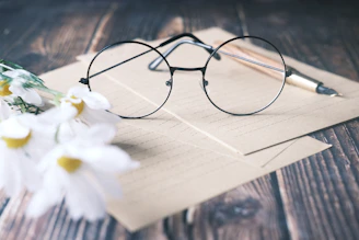 A pair of modern eyeglasses displayed on a wooden table surrounded by fresh flowers.