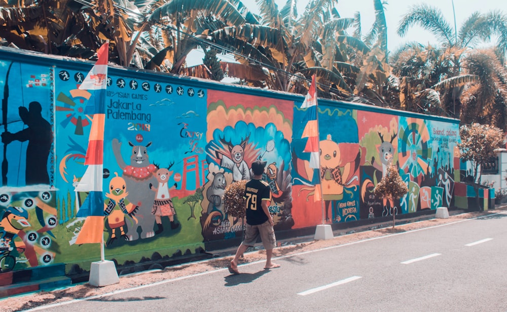 a person walking down a street next to a colorful wall