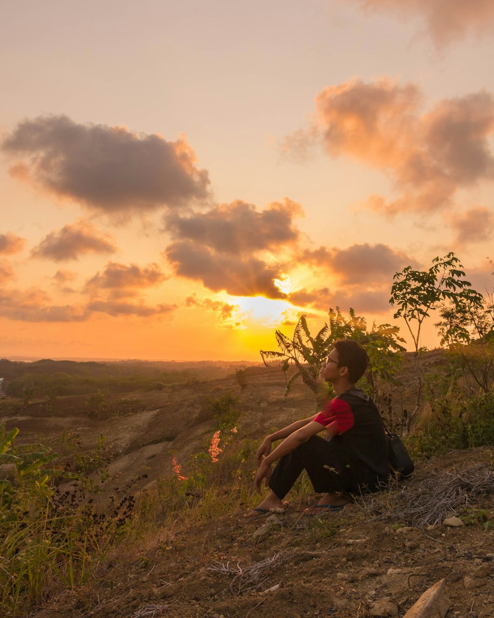 a man sitting on a hill watching the sun go down
