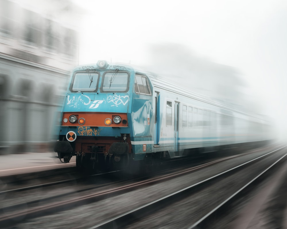 a blue train traveling down train tracks next to a tall building