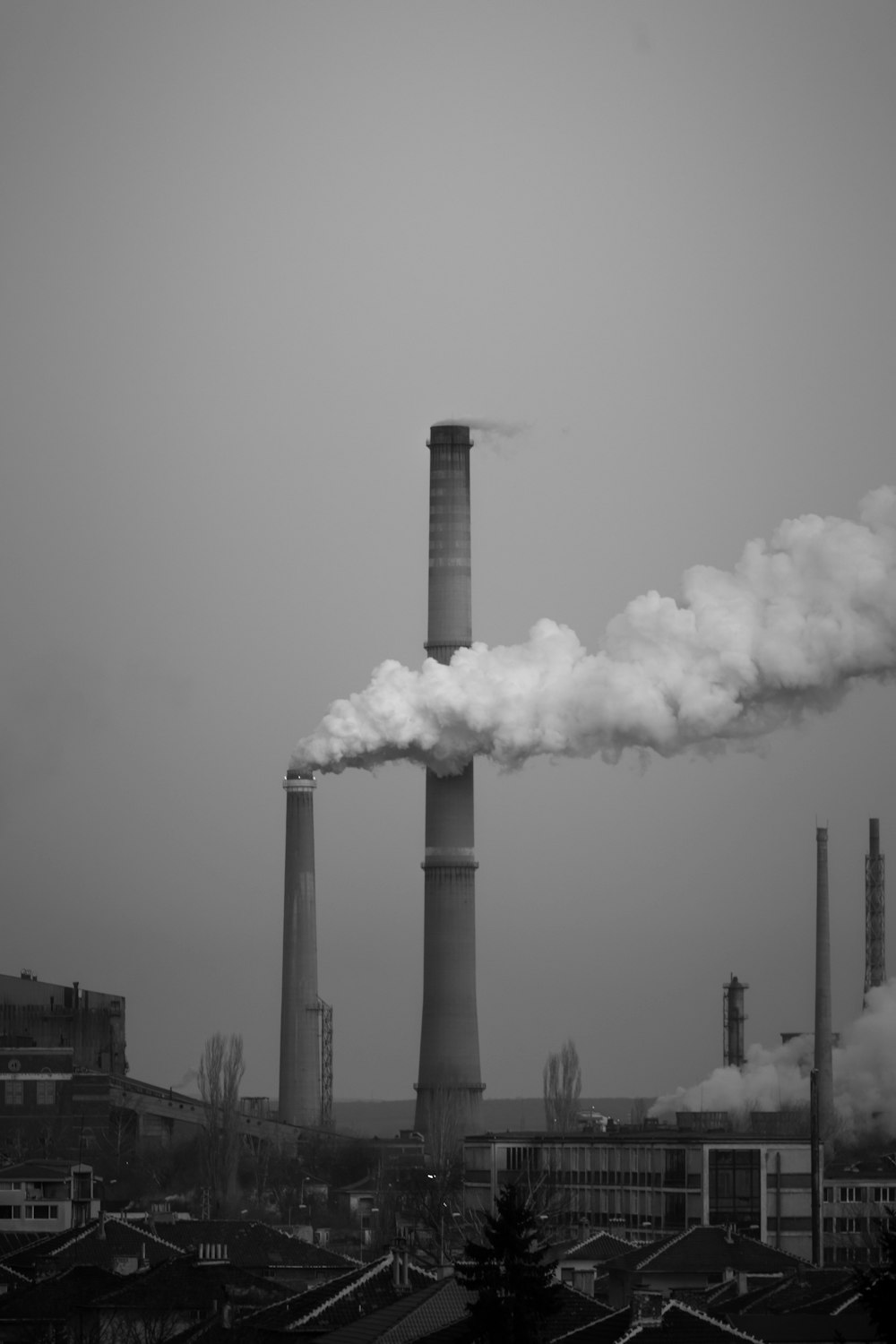 a smokestack emits from a factory in a black and white photo