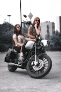 two women sitting on a motorcycle in a parking lot