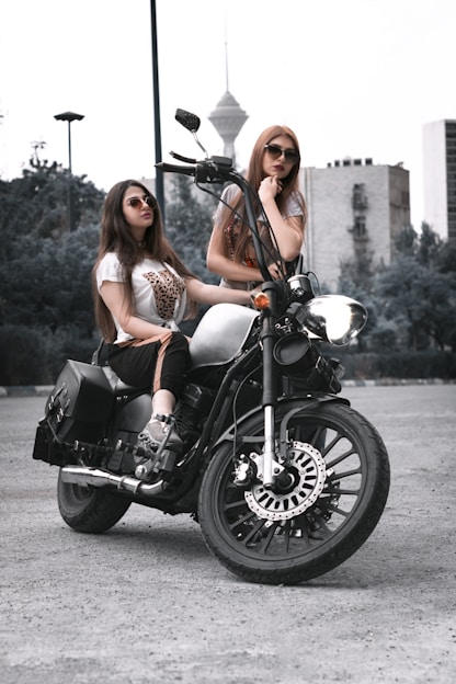 two women sitting on a motorcycle in a parking lot