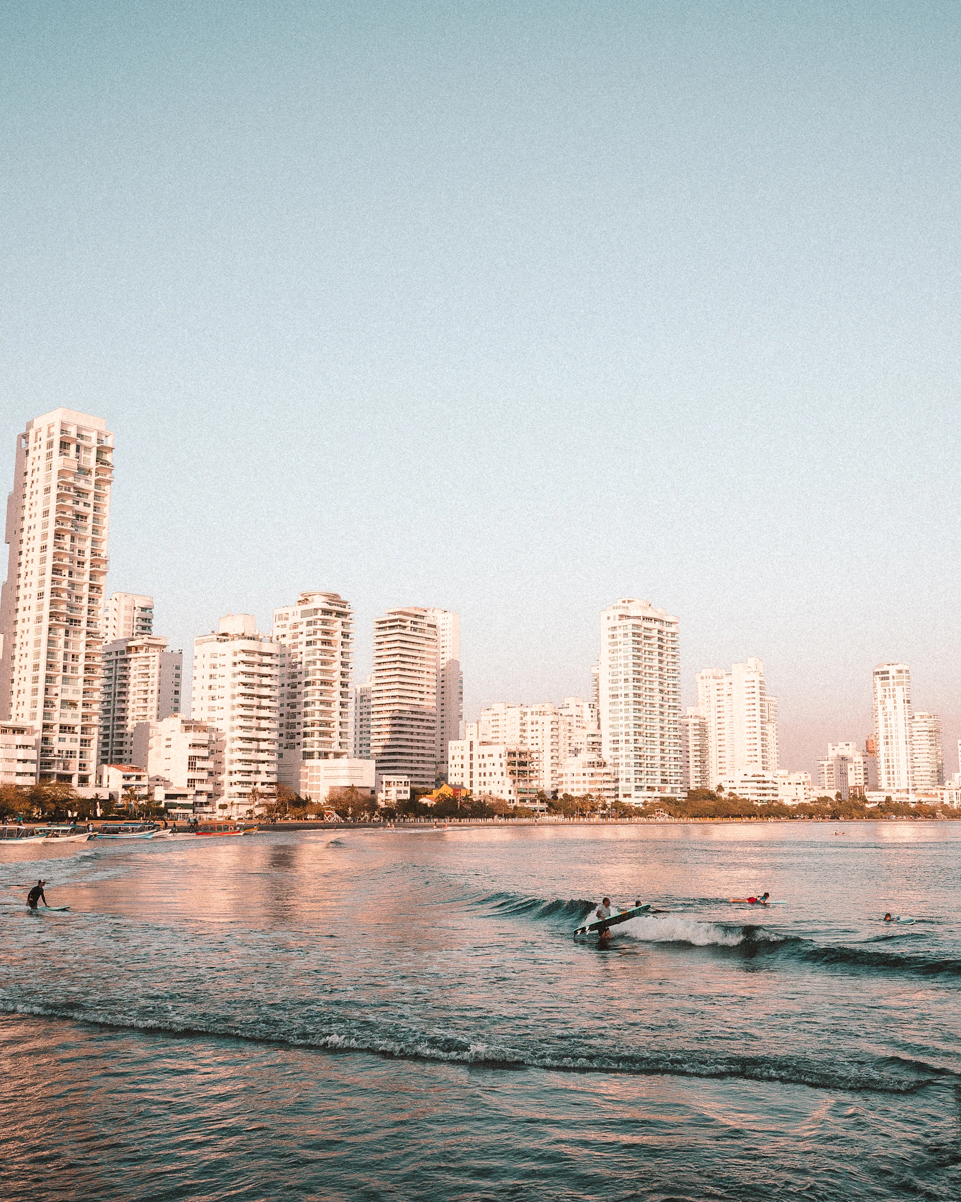 Cartagena Colombia beach at warm golden sunset light with tall white modern buildings along the shore and surfers and swimmers in the Caribbean waves