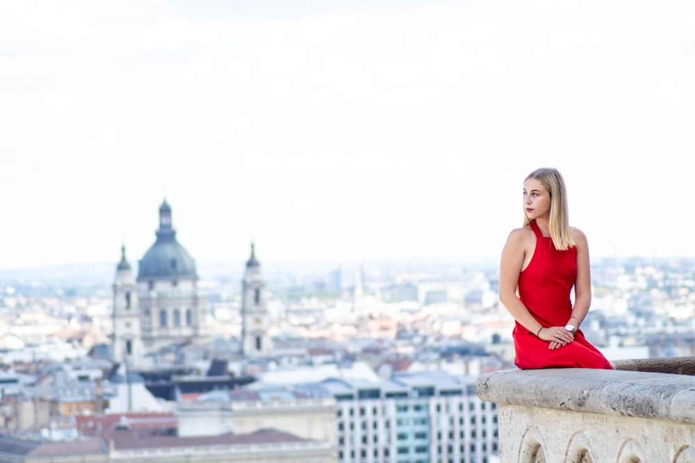 a woman in a red dress sitting on a ledge