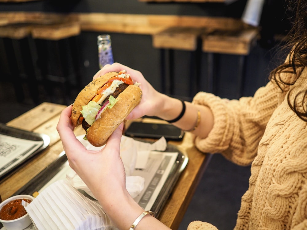 a woman sitting at a table with a sandwich in her hand