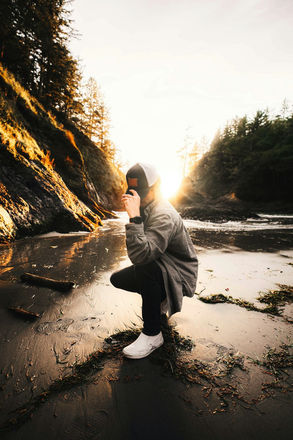 a person squatting on a beach near a body of water