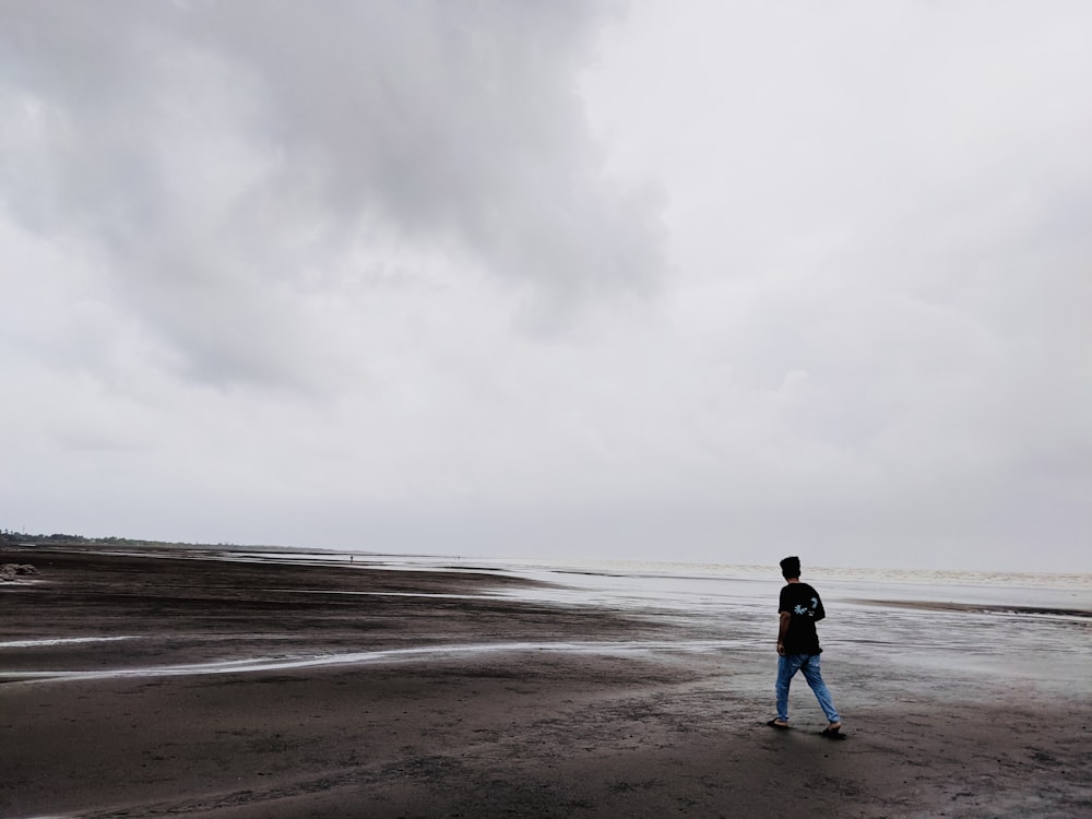a man standing on top of a sandy beach under a cloudy sky