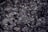 A mixture of charred debris and ash with small pieces of partially burned materials. The texture is rough and fragmented, and some areas show a metallic sheen.