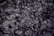 A mixture of charred debris and ash with small pieces of partially burned materials. The texture is rough and fragmented, and some areas show a metallic sheen.