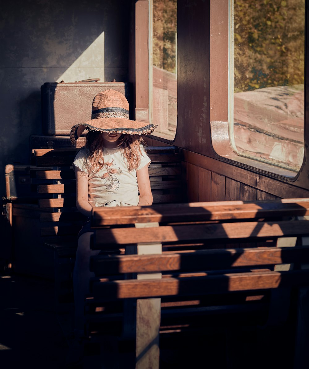 a little girl sitting on a bench wearing a hat