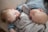Two young children are peacefully sleeping side by side, lying on a comfortable-looking surface with soft textures. They are both wearing blue and white striped pajamas. A plush, gray blanket is nestled between them, adding to the cozy atmosphere.
