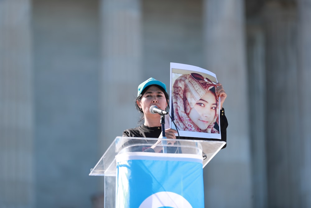 a woman standing at a podium with a picture of a woman behind her