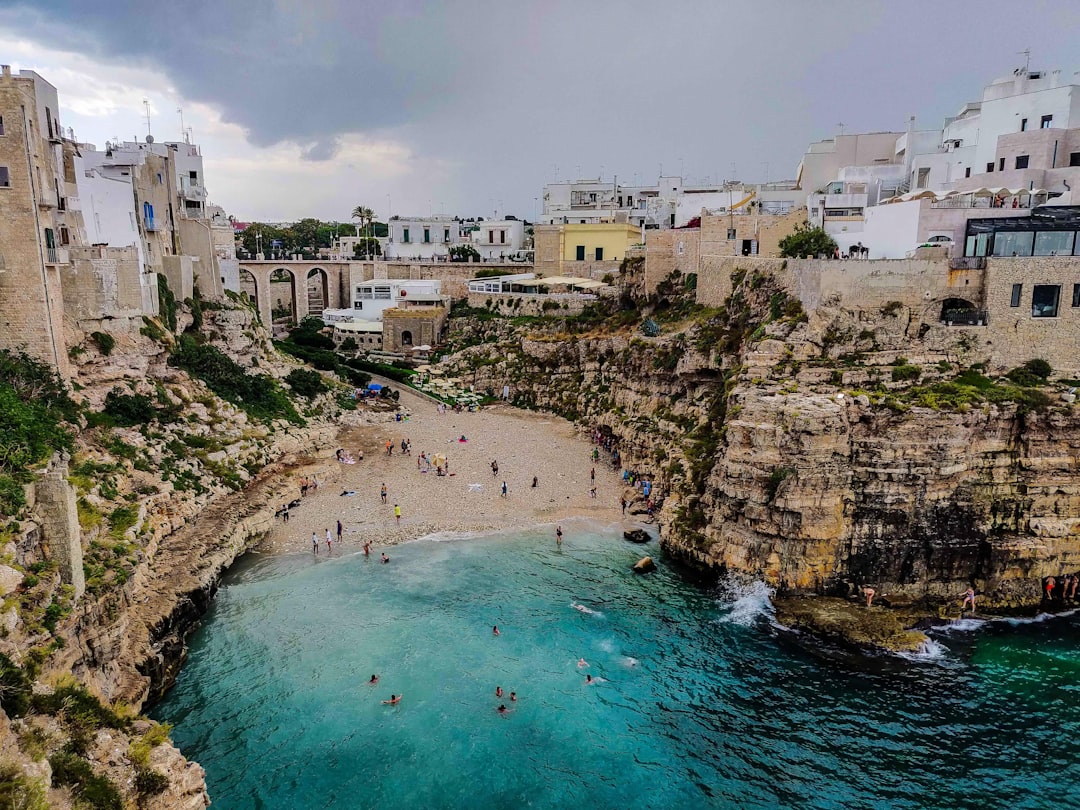 a group of people standing on top of a cliff next to a body of water, A cloudy day on an Italian beach