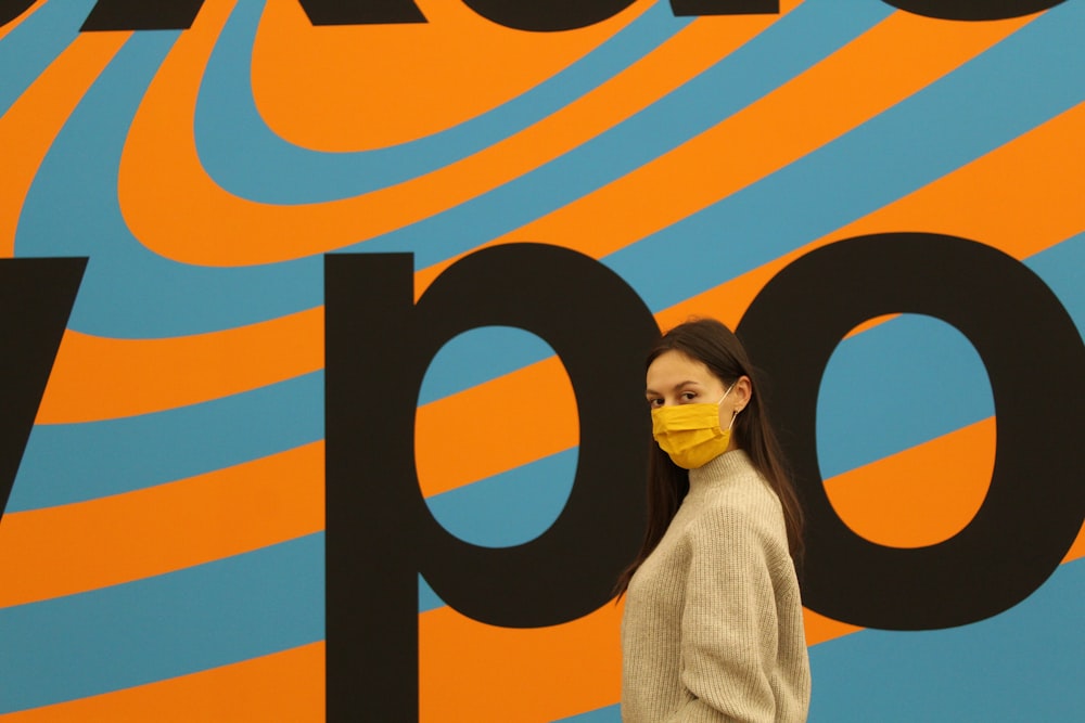 a woman wearing a face mask standing in front of a colorful wall