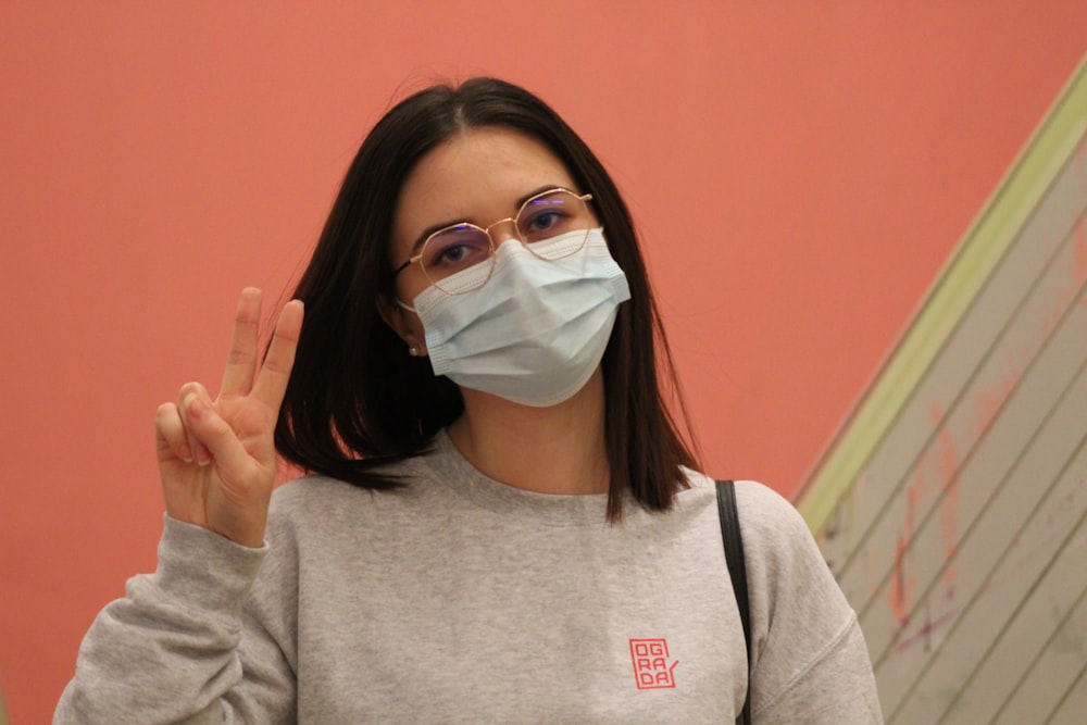a woman wearing a face mask making a peace sign