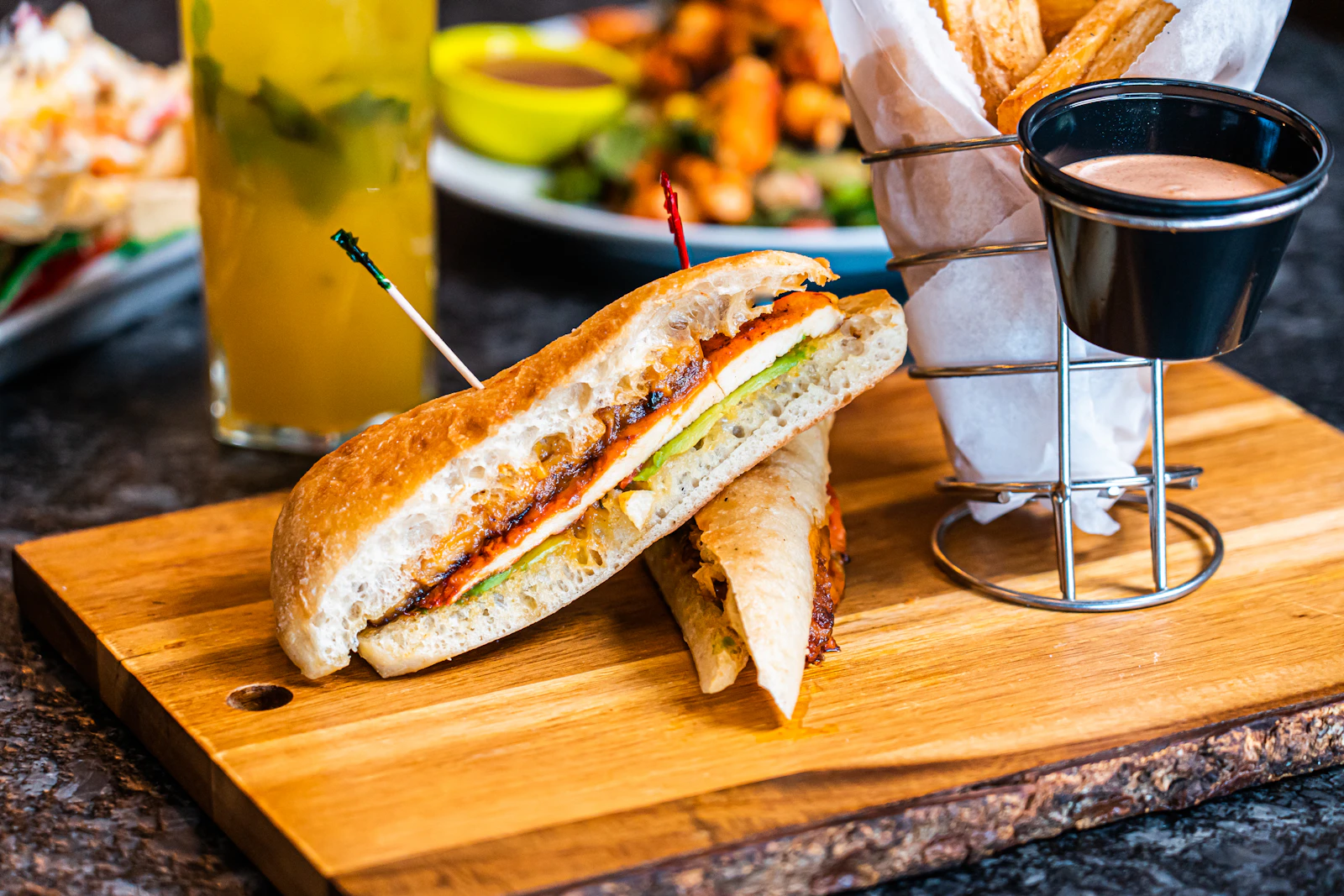 Sándwich prensado cortado a la mitad sobre tabla de madera, con queso derretido y pepinillos, junto a papas; fotografía de referencia de Unsplash
