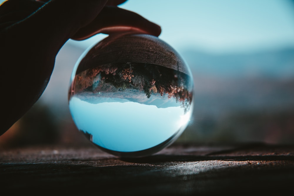 a person holding a glass ball with a mountain in it