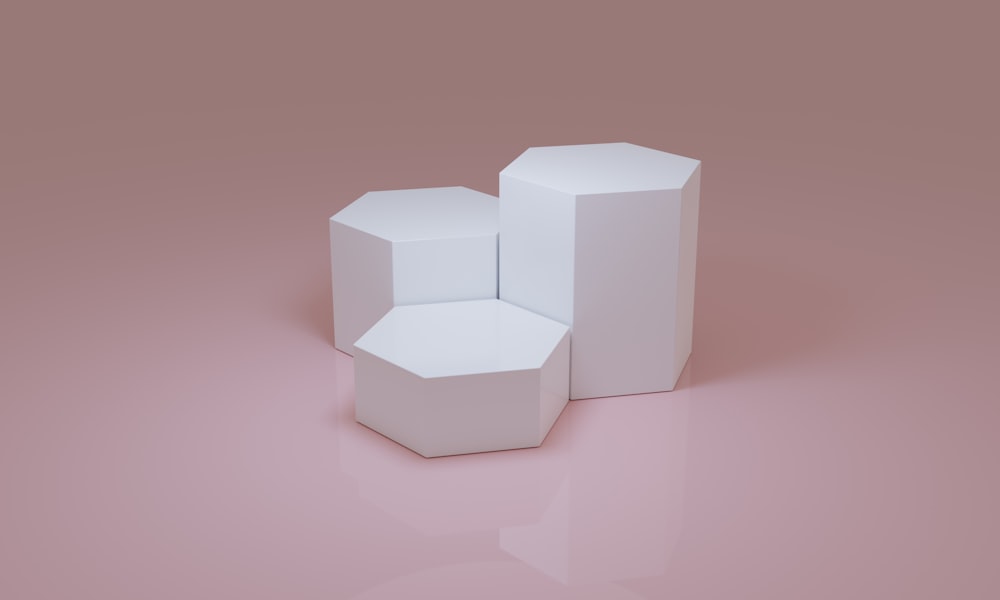 Tre scatole bianche sedute sopra una superficie rosa