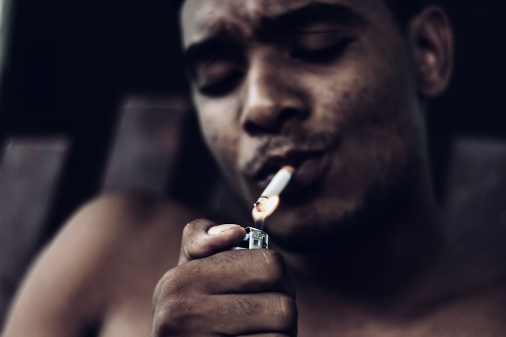 a shirtless man lighting a cigarette in his hand