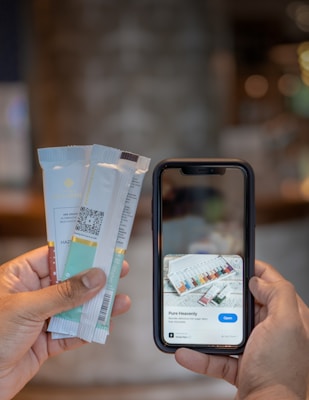 A hand holding several packaged chocolate bars is visible on the left, while another hand holds a smartphone displaying information about 'Pure Heavenly' chocolate bars with an option to open a link.