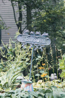 a welcome sign that has frog design in the middle of a garden