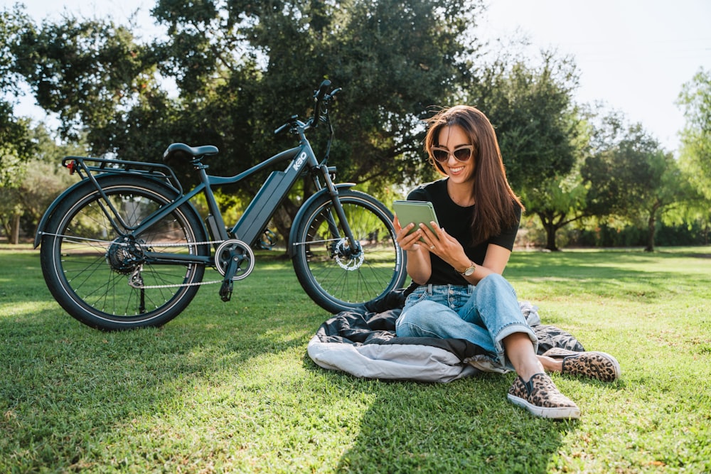 a woman sitting on the grass next to a bicycle