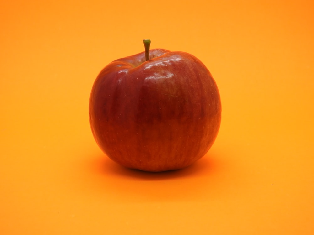 a red apple sitting on top of an orange surface