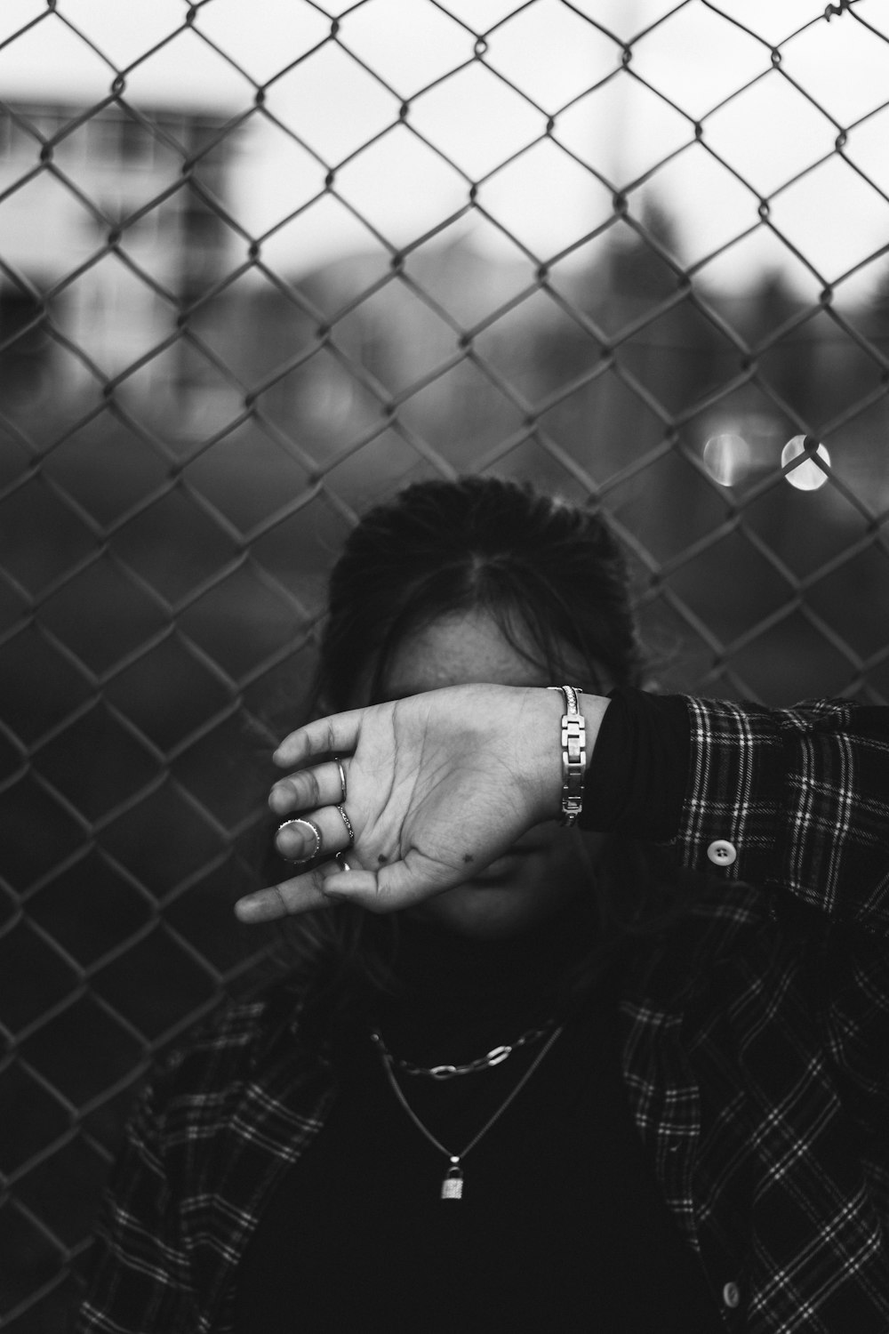 a black and white photo of a person covering their face behind a fence