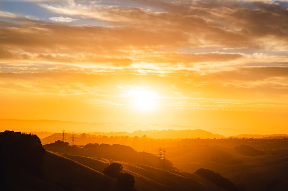 the sun is setting over a hilly area