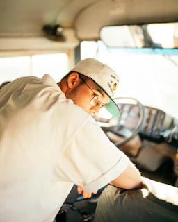 a man wearing a hat and glasses sitting in a bus