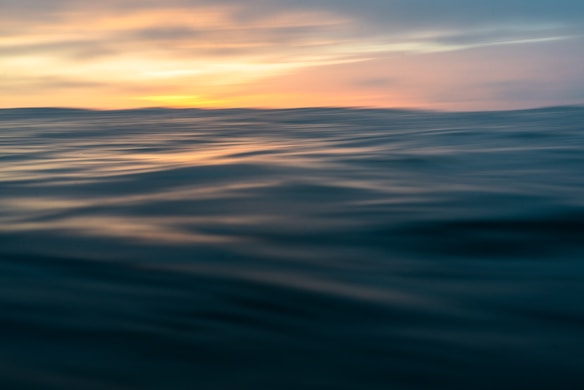 A serene ocean scene with gentle waves under a sky painted with warm hues of orange and yellow from the setting sun.
