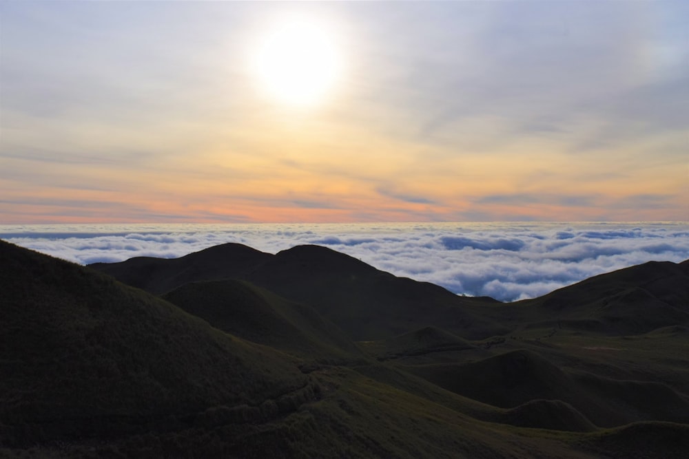 the sun is setting over the clouds in the mountains