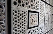 Intricate wooden panels featuring geometric and floral patterns in a repetitive layout. The carvings are detailed with various shapes, including hexagons and stars, framed by rectangular borders.