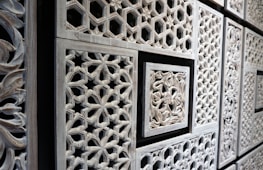 Intricate wooden panels featuring geometric and floral patterns in a repetitive layout. The carvings are detailed with various shapes, including hexagons and stars, framed by rectangular borders.