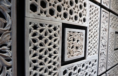 Intricate wooden panels featuring geometric and floral patterns in a repetitive layout. The carvings are detailed with various shapes, including hexagons and stars, framed by rectangular borders.
