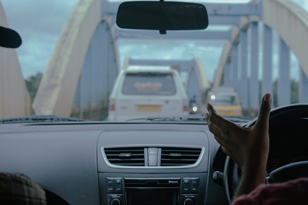 a person driving a car on a road with a bridge in the background