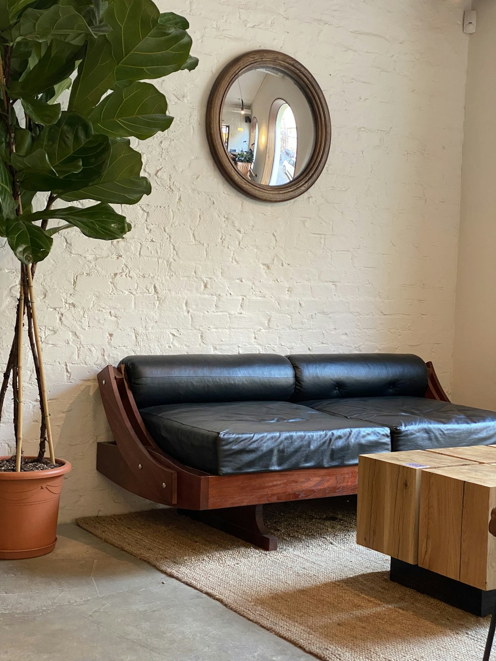 a living room with a black leather couch and a potted plant