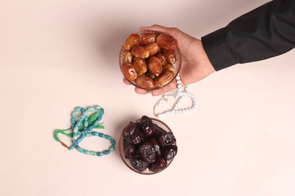 a person holding a bowl of nuts next to a string of beads